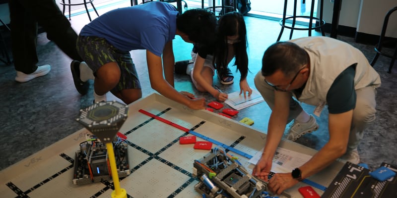 Mentors and a young builder learning together beside a robotics field